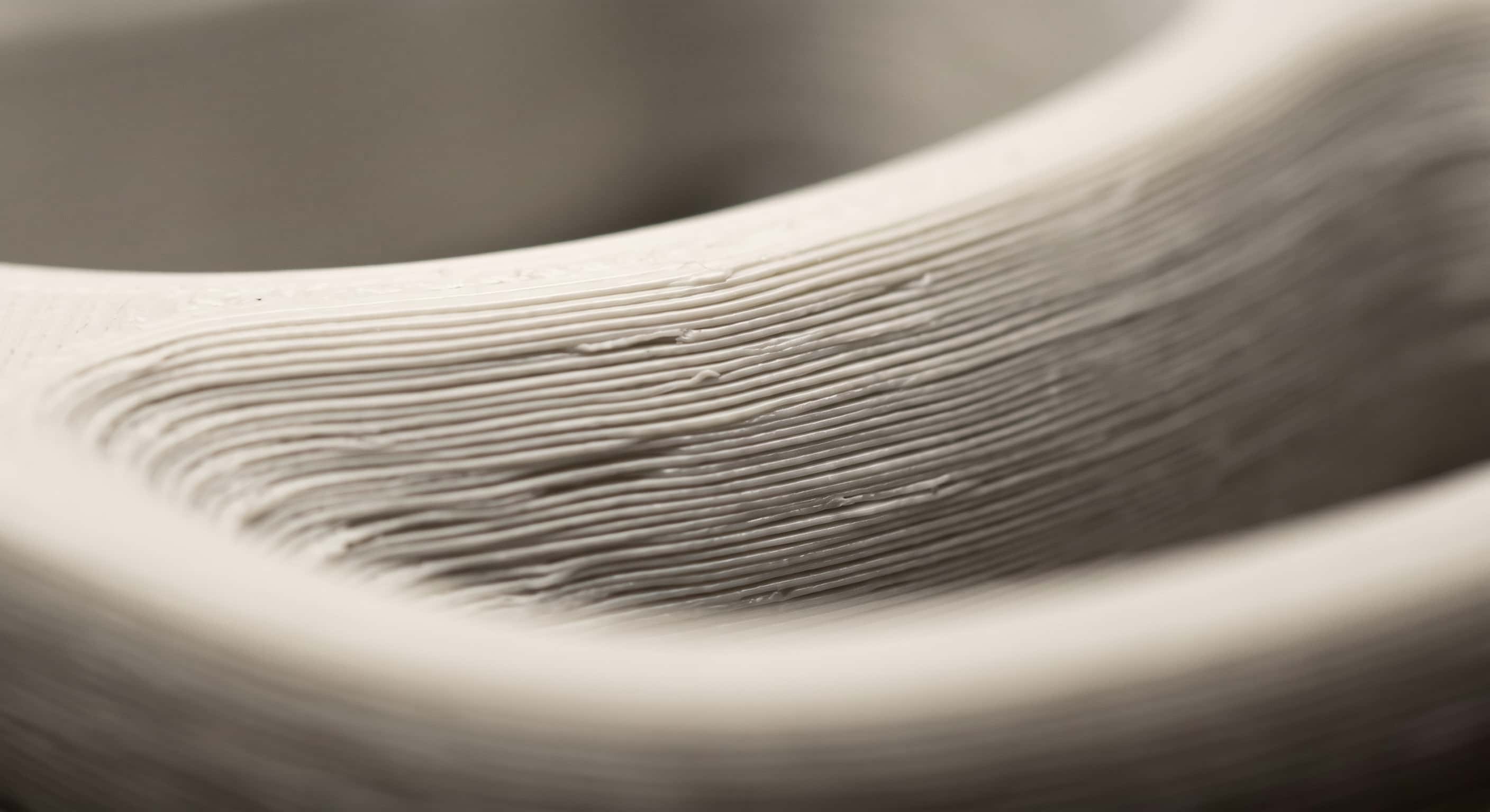 Extreme close-up of a curved off-white printed surface under raking light, its layer lines running across the curve like the grain of wood